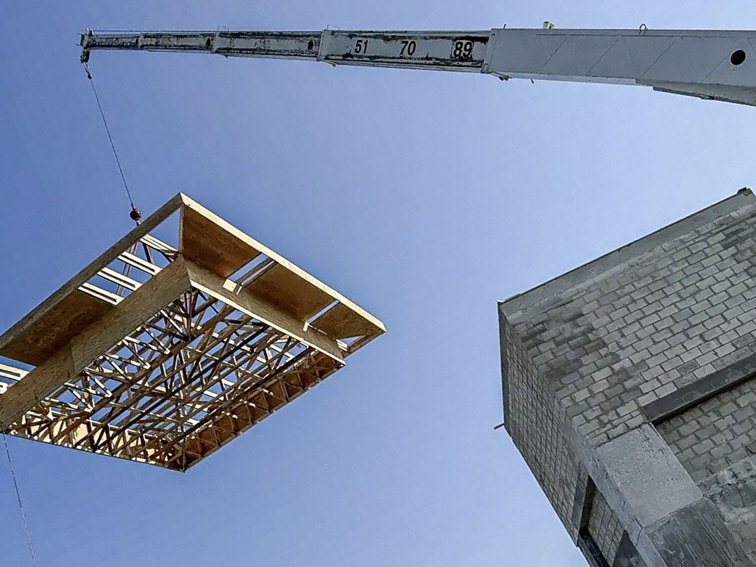 Roof assembly being lifted by crane over a masonry building